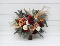 a bridal bouquet with red, orange and white flowers in front of a white wall