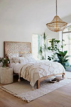 a bed with white sheets and pillows in a bedroom next to a plant on the floor