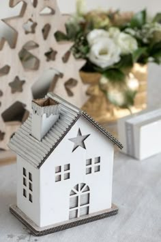 a small white house sitting on top of a table next to a vase filled with flowers