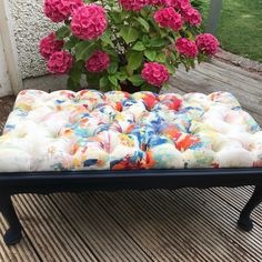 an ottoman with flowers in the background and a potted plant next to it on a deck