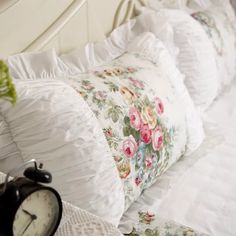 an alarm clock sitting on top of a white bed next to pillows and blankets with ruffles