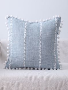 a blue and white striped pillow with pom - poms on the bottom, sitting on a couch