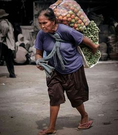 a woman walking down the street carrying lots of fruit