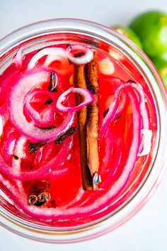 a bowl filled with red onions and cinnamon sticks next to limes on a white surface