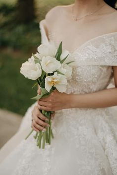 a woman in a wedding dress holding a bouquet of white tulips and greenery