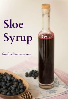 a wooden spoon with blueberries next to a bottle of sloe syrup on a table