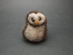 a small stuffed owl sitting on top of a gray table next to a black wall