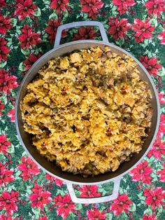 a pan filled with food sitting on top of a flowery tablecloth next to red flowers