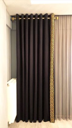 a black curtain with gold greek border hanging in front of a white radiator