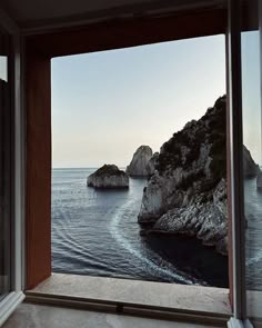 an open window looking out at the ocean and rocks in the water from inside a house