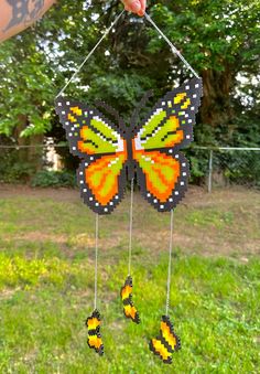 a hand is holding up a colorful butterfly mobile in front of some grass and trees