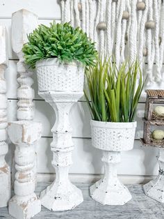 three white vases with plants in them sitting on a table next to other decorative items