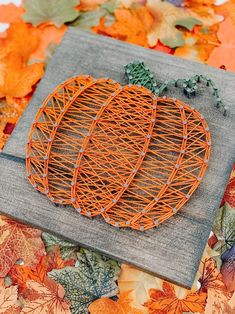 an orange wire pumpkin sitting on top of a wooden cutting board surrounded by autumn leaves