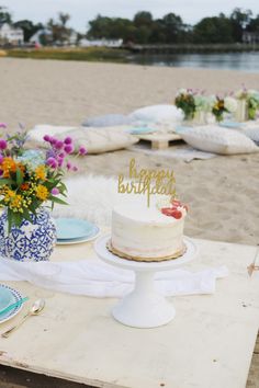 a birthday cake sitting on top of a wooden table next to flowers and plates in front of it