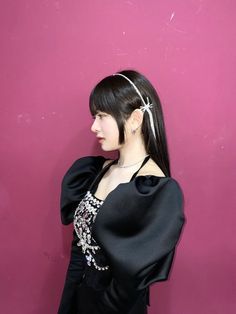 a woman wearing a black dress with a bow in her hair standing against a pink wall