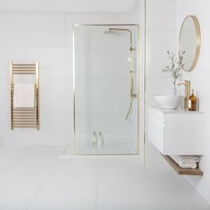 a bathroom with white tile and gold accents on the shower, sink, and mirror