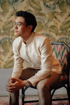 a man sitting on top of a chair in front of a wallpapered room