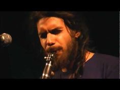 a man with long hair and beards is playing a flute in front of a microphone