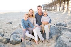 a man, woman and two children are sitting on rocks at the beach with a pier in the background