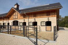 a horse barn with an open gate in front of it and a clock on the top of the building