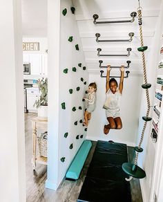 two children climbing up the side of a wall in a room with white walls and wood floors