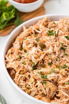 a white bowl filled with shredded chicken and garnished with parsley