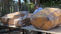 a man sitting on top of a wooden table next to large cardboard boxes in front of him