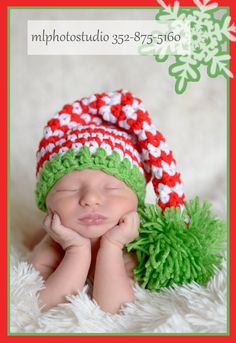 a newborn baby wearing a green and red knitted hat with pom - poms