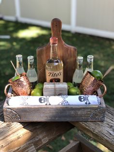 a wooden tray with bottles and glasses in it sitting on top of a picnic table