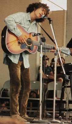 a man standing on top of a stage holding a guitar and singing into a microphone