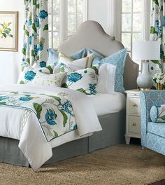 a bed with blue and green flowers on it in a bedroom next to two windows