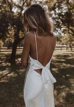 the back of a woman wearing a white dress with a bow at the waist and straps