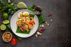 a white plate topped with food next to two bowls filled with fruit and vegetables on top of green leaves