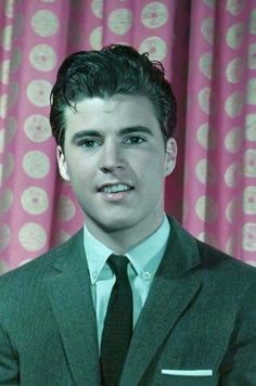 a young man in a suit and tie posing for a photo with pink curtains behind him