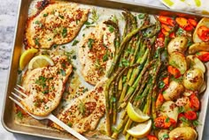 chicken, asparagus and potatoes in a pan with lemon wedges on the side