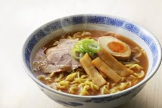 a bowl of ramen with noodles, meat and an egg on the top is sitting on a table