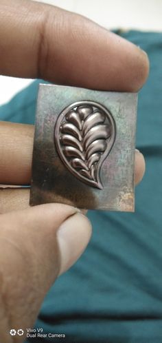 a person holding a metal object in their left hand and wearing a ring with a leaf design on it