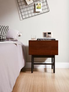 a nightstand with a phone on it next to a bed and pictures hanging on the wall