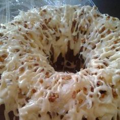 a bundt cake with white frosting and nuts on top sitting in a plastic container