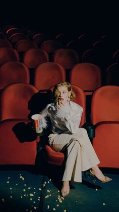 a woman sitting on a chair in front of an empty theater seat with popcorn scattered around her