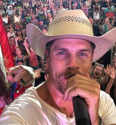 a man with a cowboy hat on singing into a microphone in front of an audience