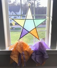 three different colored paper stars hanging from a window sill