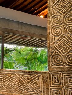 an intricately carved wall with palm trees in the background and a window to another room