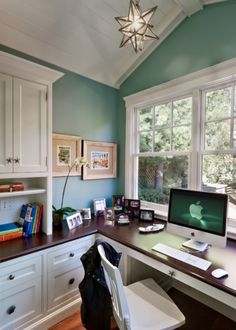 a desk with a computer on top of it in front of a window and bookshelf