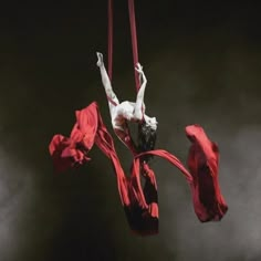 a woman is suspended in the air on a rope with red cloths around her