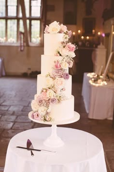 a white wedding cake with pink and white flowers on it sitting on top of a table