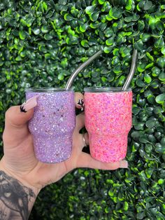 two glitter tumblers are held in front of a hedge