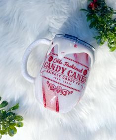 a candy cane coffee mug sitting on top of a white fur covered floor next to greenery