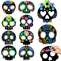 a hand holding a paintbrush next to a set of skull cutouts with different colors