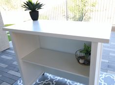 a white shelf sitting on top of a tiled floor next to a potted plant